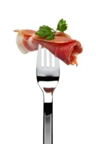 roll of dry-cured spanish serrano ham sticked on fork, garnished with parsley, isolated on white